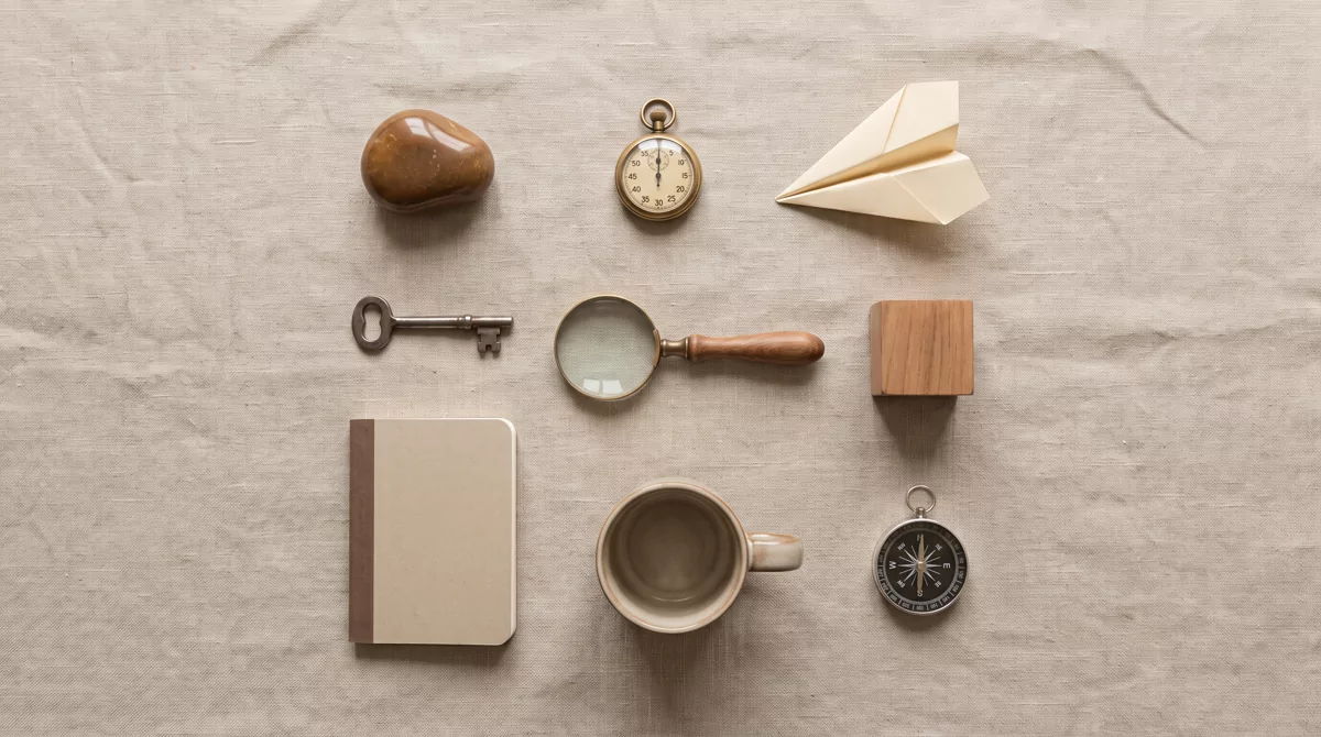 Overhead shot of nine small objects arranged in a loose grid on a linen surface, including a stopwat
