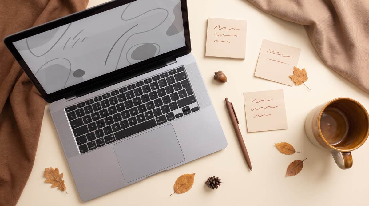 An overhead flat-lay of a tidy desk with a laptop displaying abstract placeholder lines, sticky note