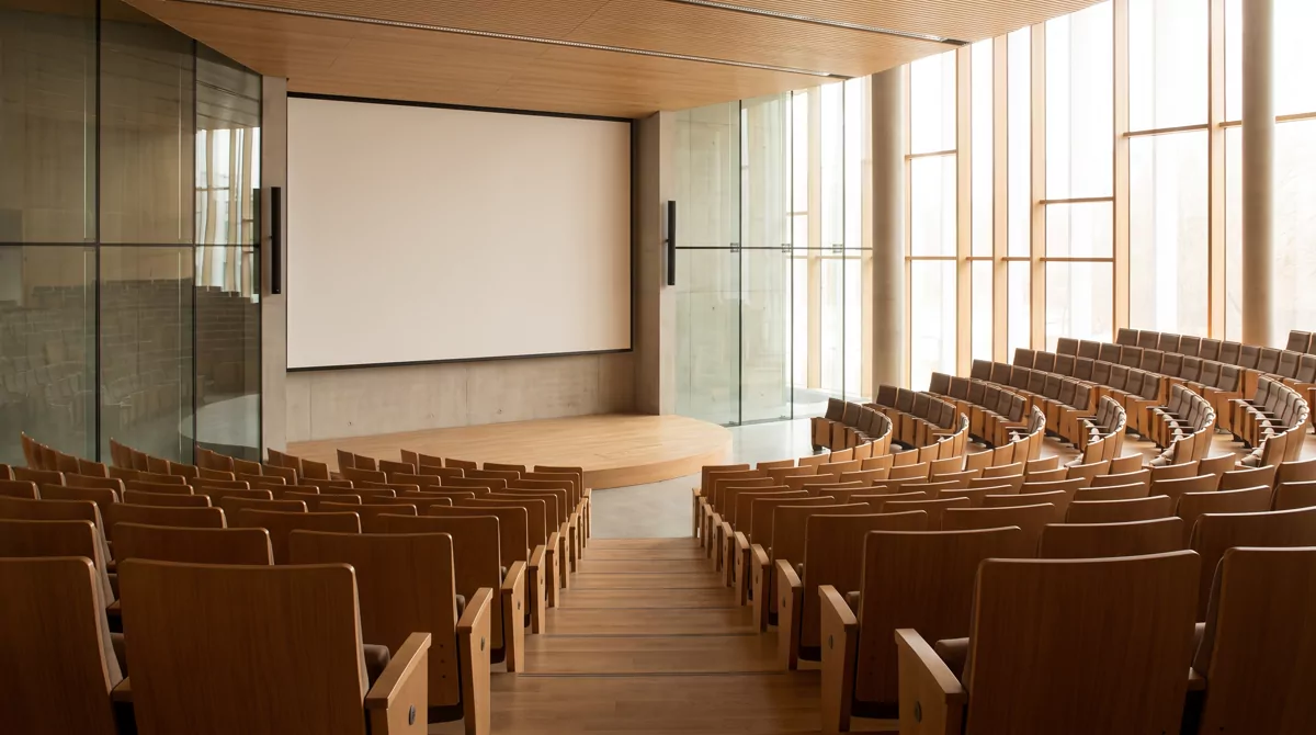 An empty modern lecture hall with warm wood seating and soft window light, no people, no signage