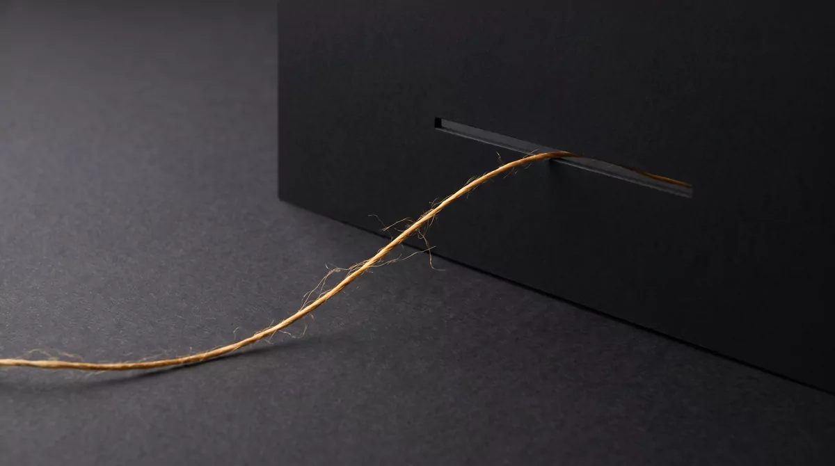 Abstract studio composition on a dark charcoal background: a single warm gold thread passing through